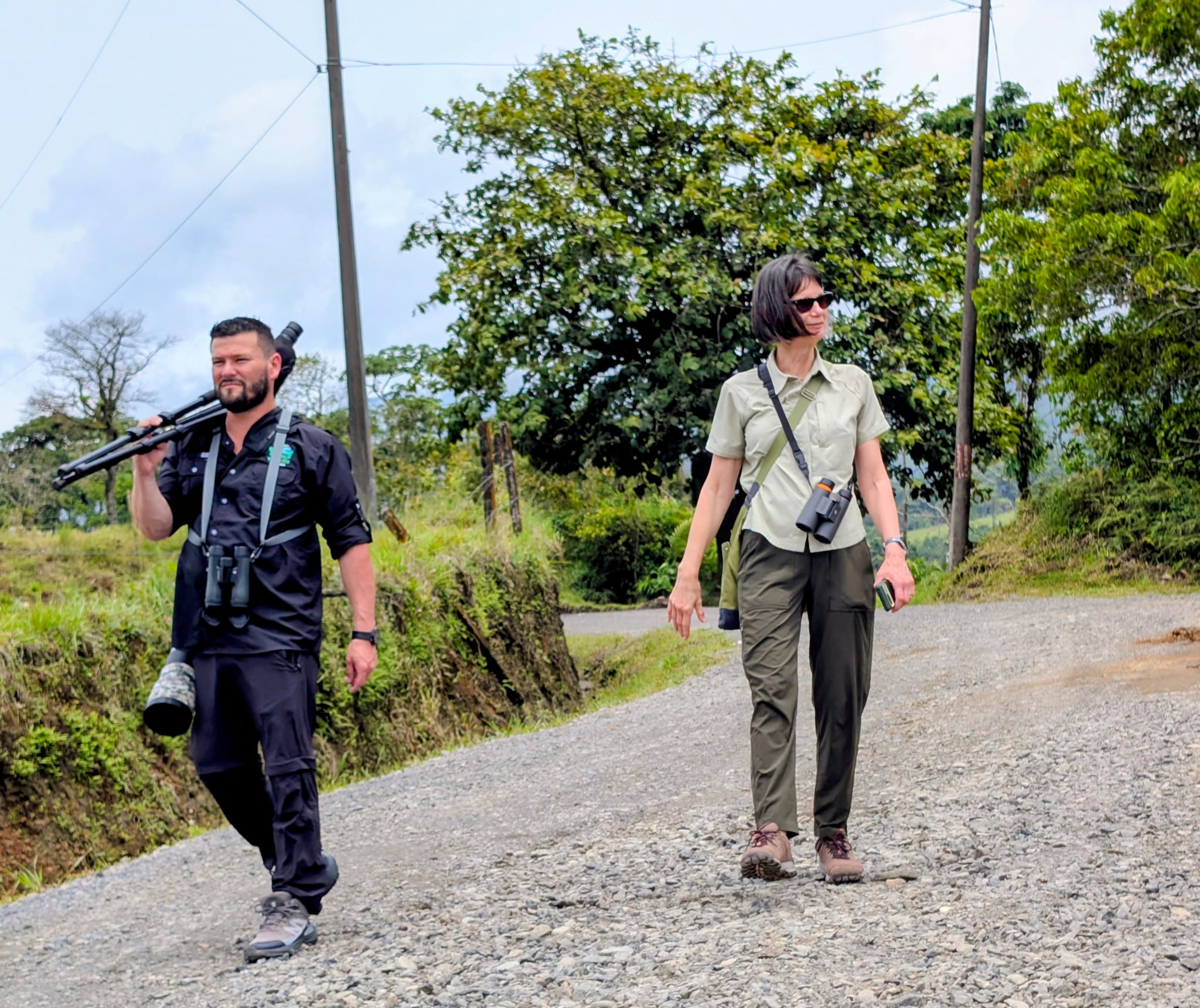 Michael carrying a spotting scope while birding a quiet country road with a guest