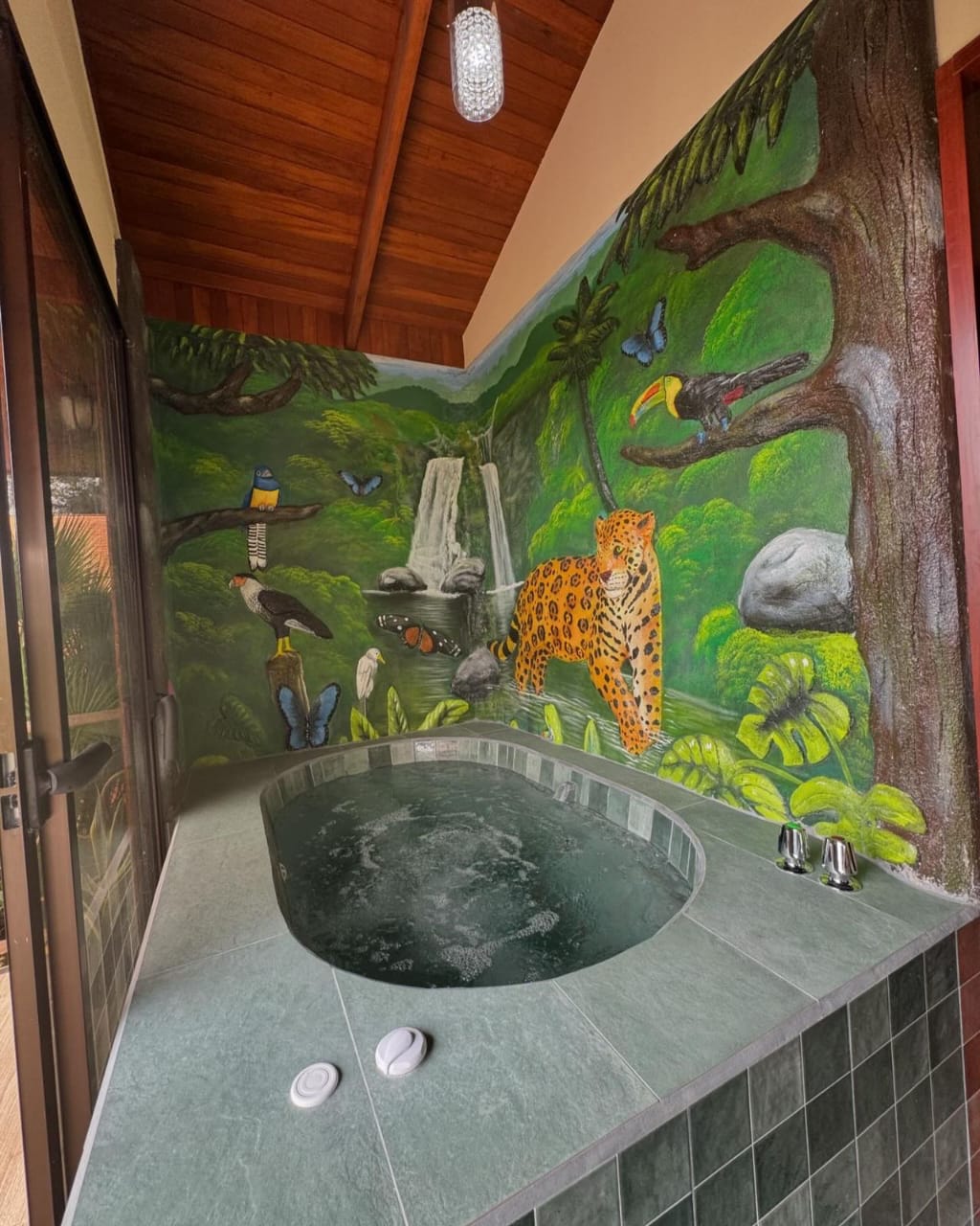 Private jacuzzi tub in front of a hand-painted rainforest mural with toucans and a jaguar